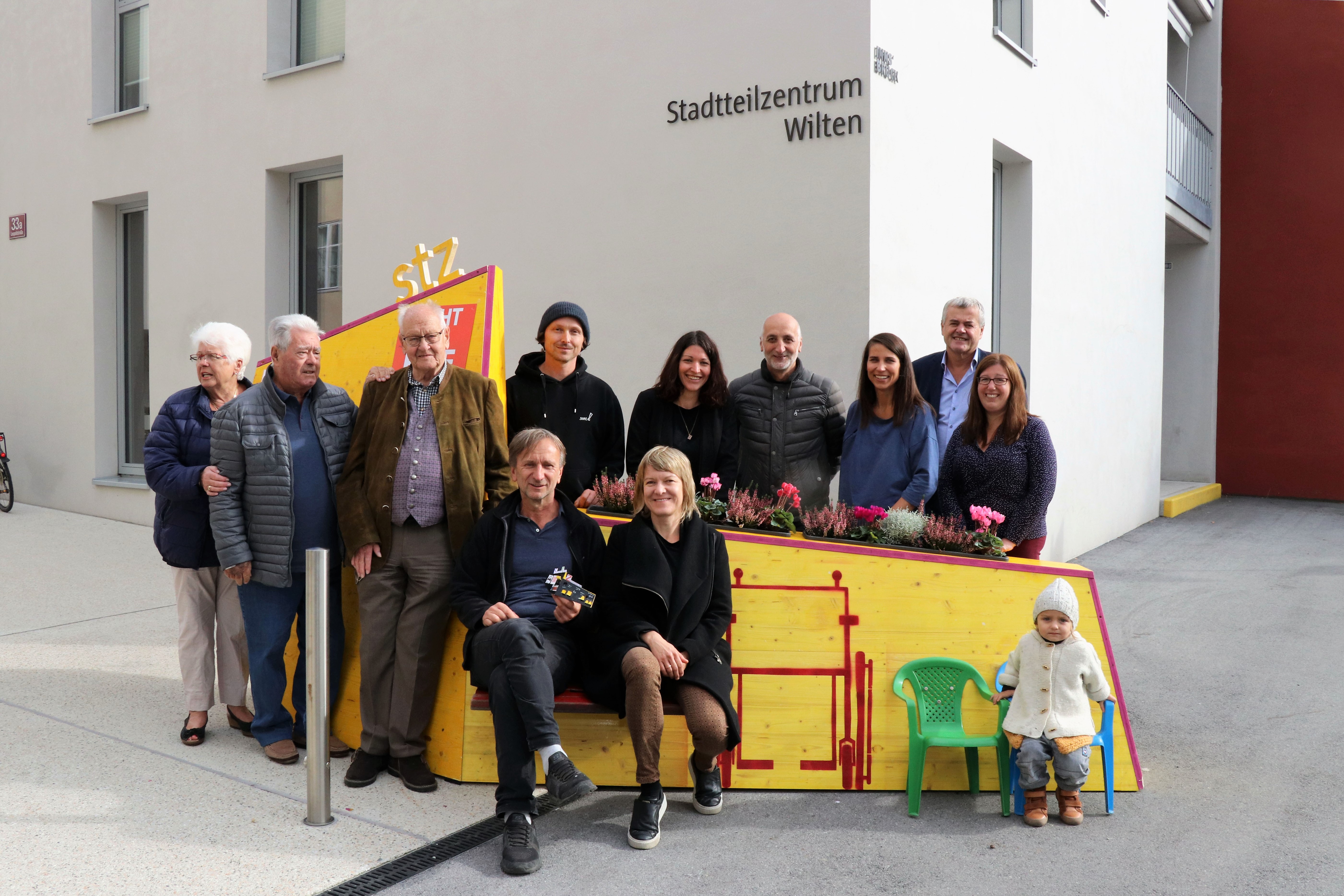Kreativ, bunt und unübersehbar – so präsentiert sich seit 4. Oktober das temporäre, öffentliche Möbelstück vor dem Stadtteilzentrum Wilten in der Leopoldstraße 33a. Die Idee für das hölzerne Bauwerk entstand im Rahmen eines Beteiligungsprozesses bereits im Dezember 2017. Damals kamen NachbarInnen, ein Kreativteam aus Wilten und VertreterInnen des Stadtteilzentrums zusammen, um über die Gestaltung des Innenhofes zu beratschlagen. Die nun realisierte Konstruktion enthält die gewünschten Elemente, bestehend aus Beschriftung, Informations- und Plakatflächen, einem Buchtauschregal, Sitzgelegenheiten und kann mit Blumentöpfen ausgestattet werden. Bei der Einweihung kamen viele Beteiligte und UnterstützerInnen zusammen, unter ihnen auch Gemeinderätin Janine Bex, Geschäftsführer Hubert Innerebner (Innsbrucker Sozialen Dienste, ISD), Stadtteilkoordinatorin Florence Fritz sowie das Kreativteam rund um Charly Walter und zahlreiche AnrainerInnen. Bis Juni 2021 lädt das öffentliche Möbelstück vor dem Stadtteilzentrum Wilten zum Verweilen und Verwenden ein. AA