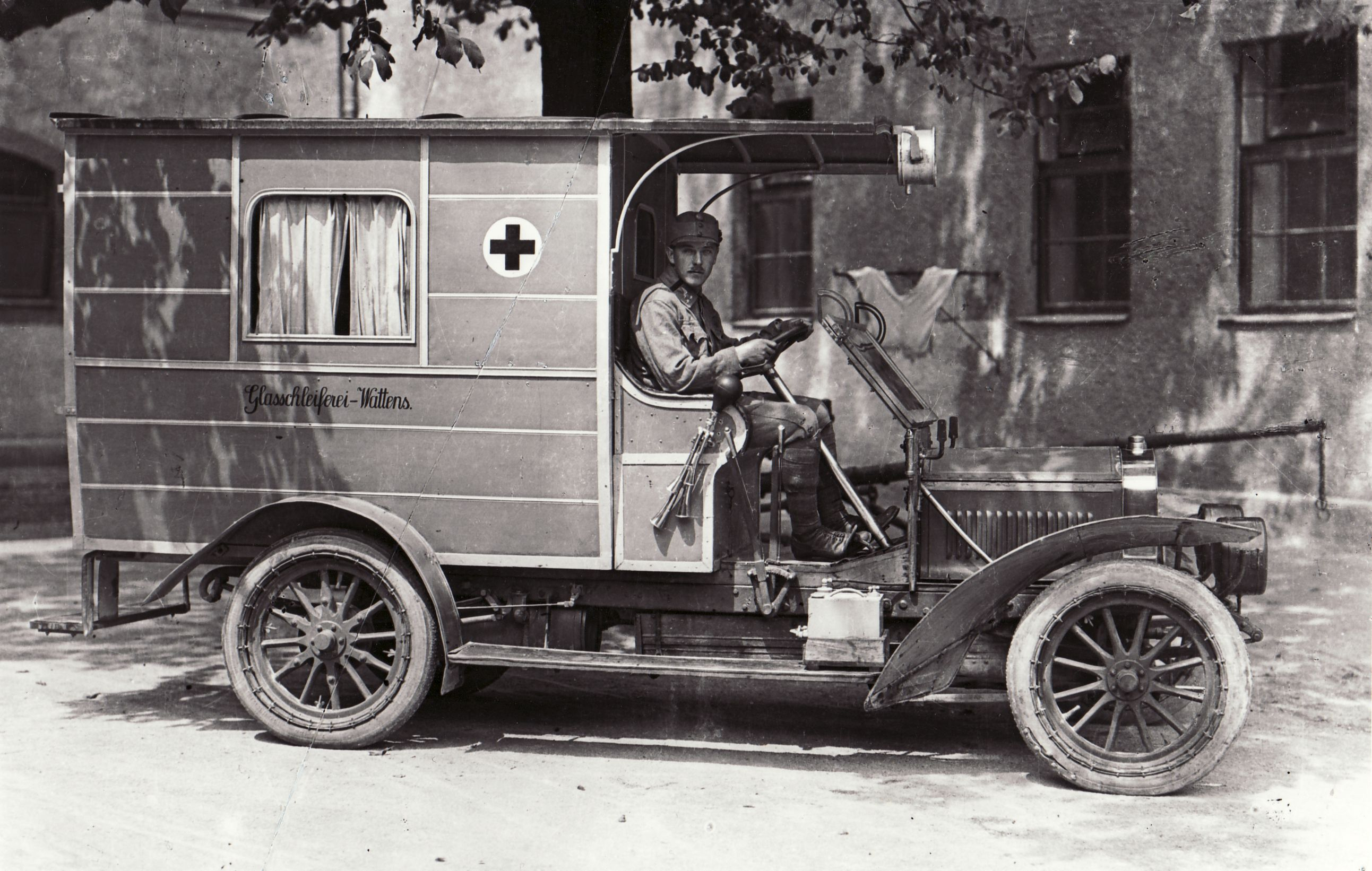 Der erste Sanitätskraftwagen der Rettungsabteilung der Freiwilligen Feuerwehr Innsbruck vor der Rettungsstation im Rathaus. Auf der Aufnahme sind die Adaptierungen der Rettungsabteilung zu sehen: Außenbatterie, elektrische Scheinwerfer und eine anders gestaltete Hupe.