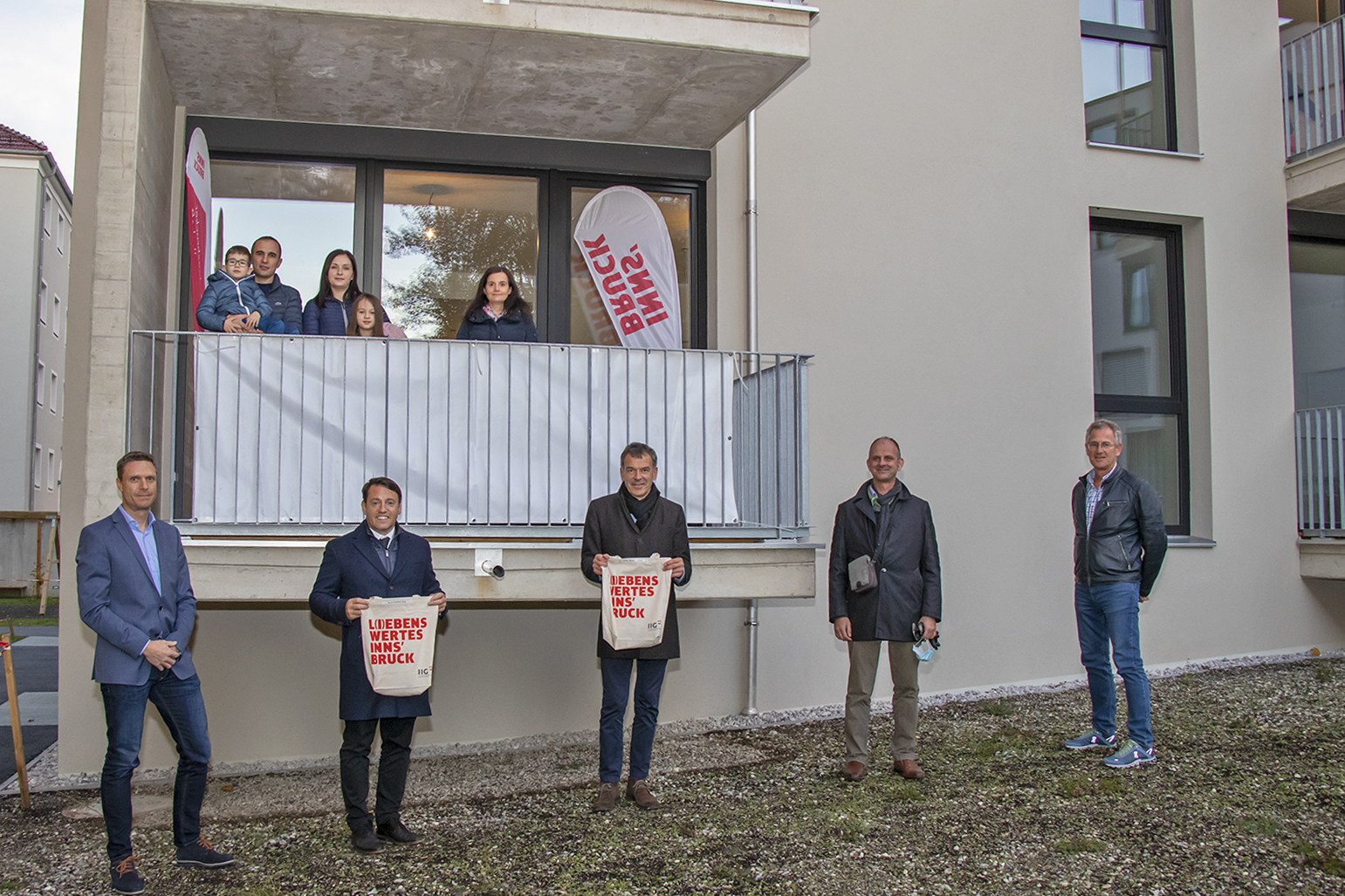 Eine vierköpfige Familie (Balkon, l.) sowie eine weitere Bewohnerin (Balkon, r.) freuen sich gemeinsam mit (vorne, v. l.) IIG-Geschäftsbereichsleiter Bernhard Matt, IIG-Geschäftsführer Franz Danler, Bürgermeister Georg Willi, Martin Franzmair (IIG-Projektleiter) und Nikolaus Reitmeir (IIG-Bauleitung) über ihr neues Zuhause in der Kranewitterstraße.