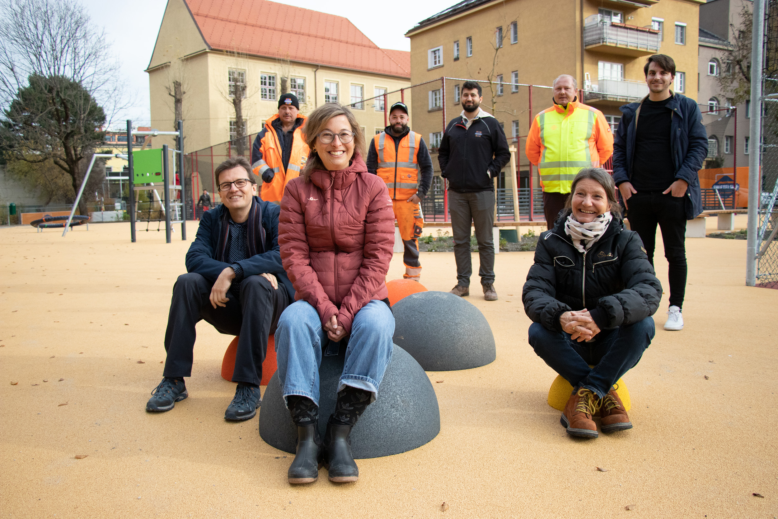 Stolz auf den neuen Spiel- und Sportplatz (sitzend v.l.): Markus Pinter, Lisa Stöllnberger (Grünanlagen Planung und Bau) und Stadträtin Uschi Schwarzl sowie (stehend; hintere Reihe) Mitarbeiter der ausführenden Baufirma und Stadtteilkoordinator Christoph Hackl vom Stadtteiltreff Pradl (ganz rechts).