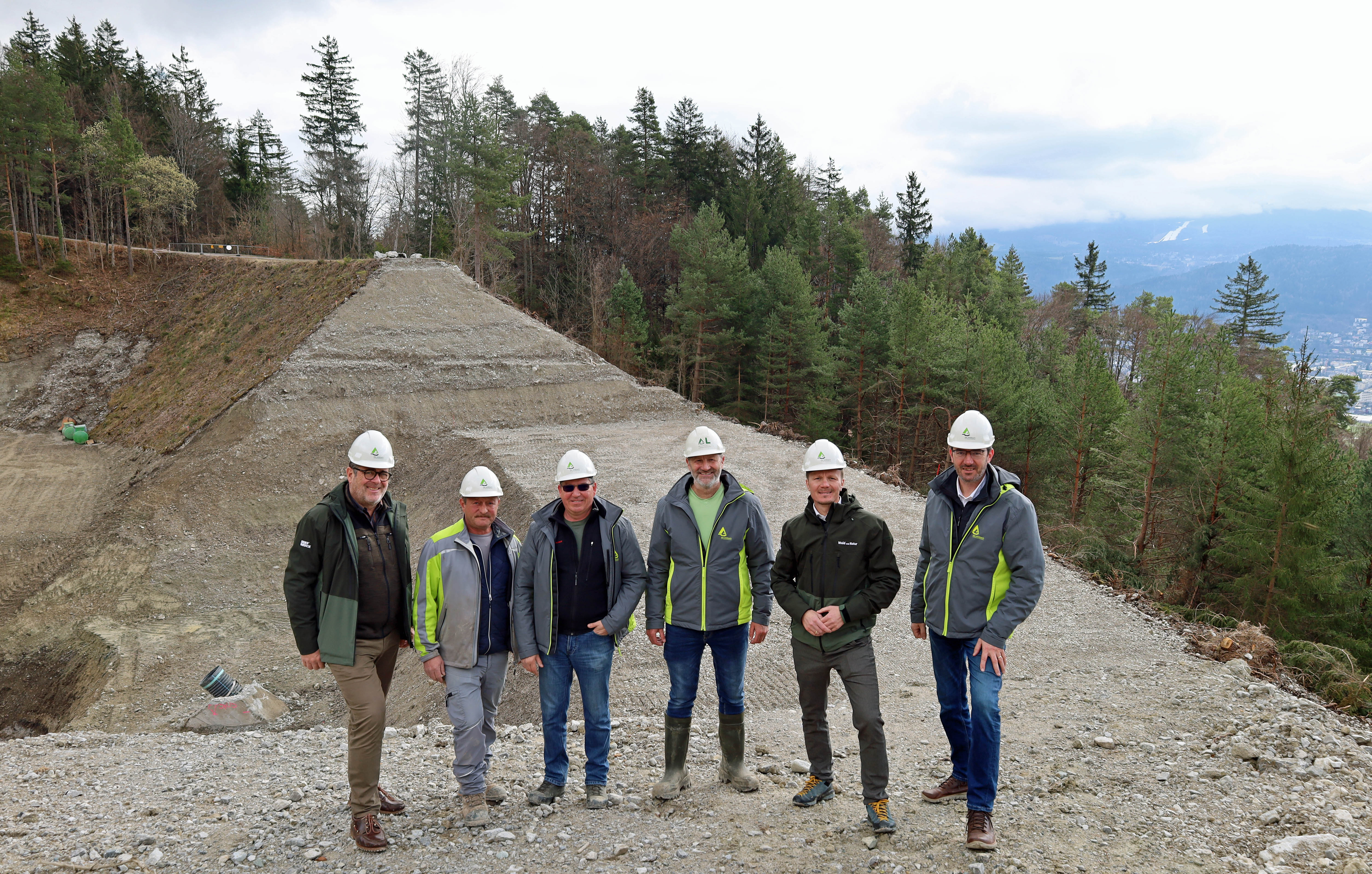 Vizebürgermeister Johannes Anzengruber (2.v.r.), Amtsleiter Andreas Wildauer (Wald und Natur, l.) und Sektionsleiter Gebhard Walter (Wildbach- und Lawinenverbauung, r.) begrüßen gemeinsam mit Mitarbeitern der WLV die Sanierung des Lawinenauffangdamms.
