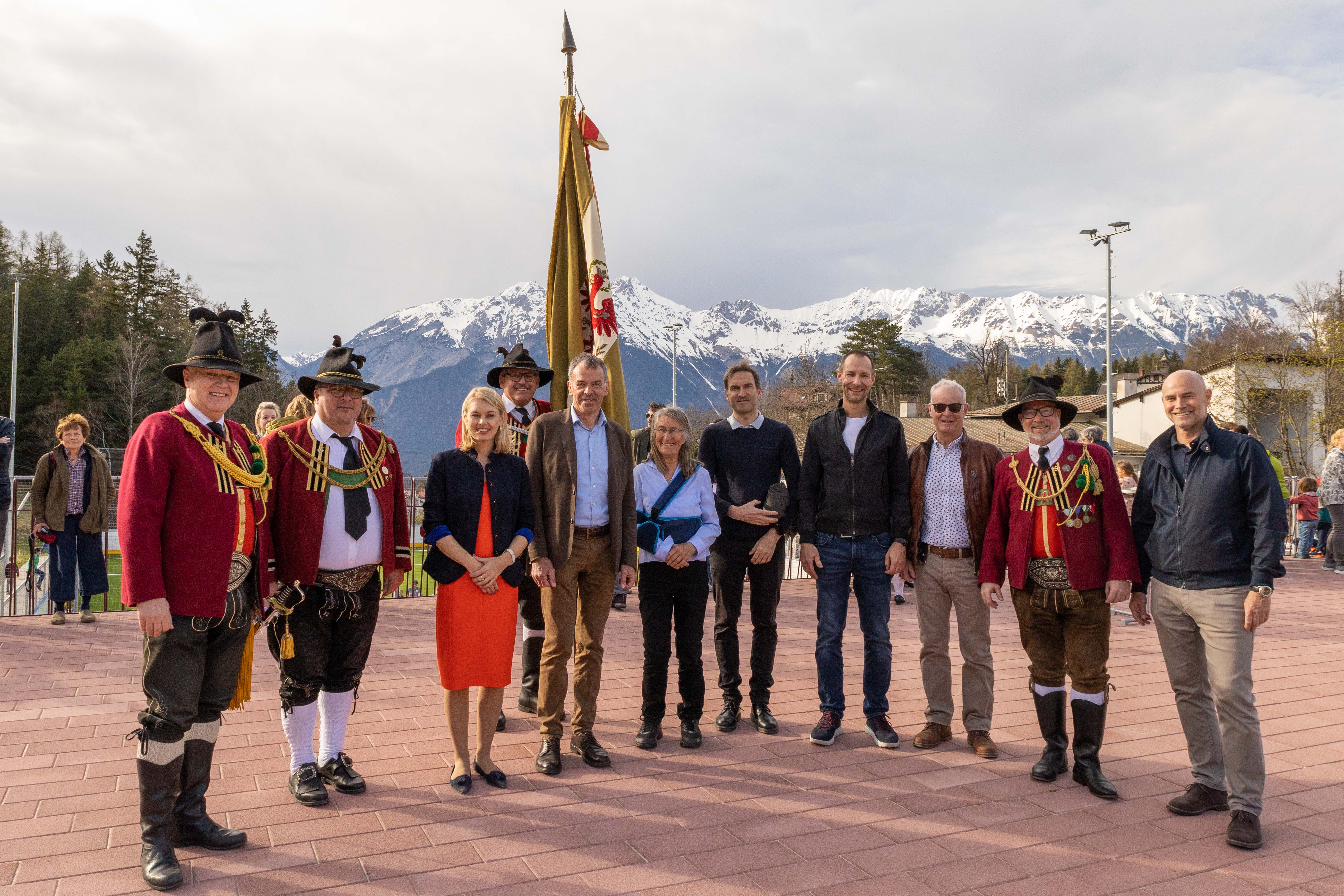 Start des Sommerbetriebes Sportanlage Zimmerwiese Igls: Innsbrucks Bürgermeister Georg Willi (5. v. l.), Sportstadträtin Elisabeth Mayr (3.v.l.), Sportamtsleiter Romuald Niescher (r.), Maria Zimak (Unterausschuss Igls,  6. v. l.), Obmann Karl Zimmermann (3. v. r., Agrargemeinschaft Igls), Hauptmann Christoph Wegscheider (Schützenkompanie Igls-Vill, l.) und Obmann Herwig Zöttl (2. v. r.) Kapellmeister Klaus Graf von der Musikkapelle Igls-Vill (2. v. l.) sowie Vertreter der Innsbrucker Immobiliengesellschaft und des Architekturbüros stimmten sich beim Eröffnungsfest auf die sportliche Sommersaison in Igls ein.