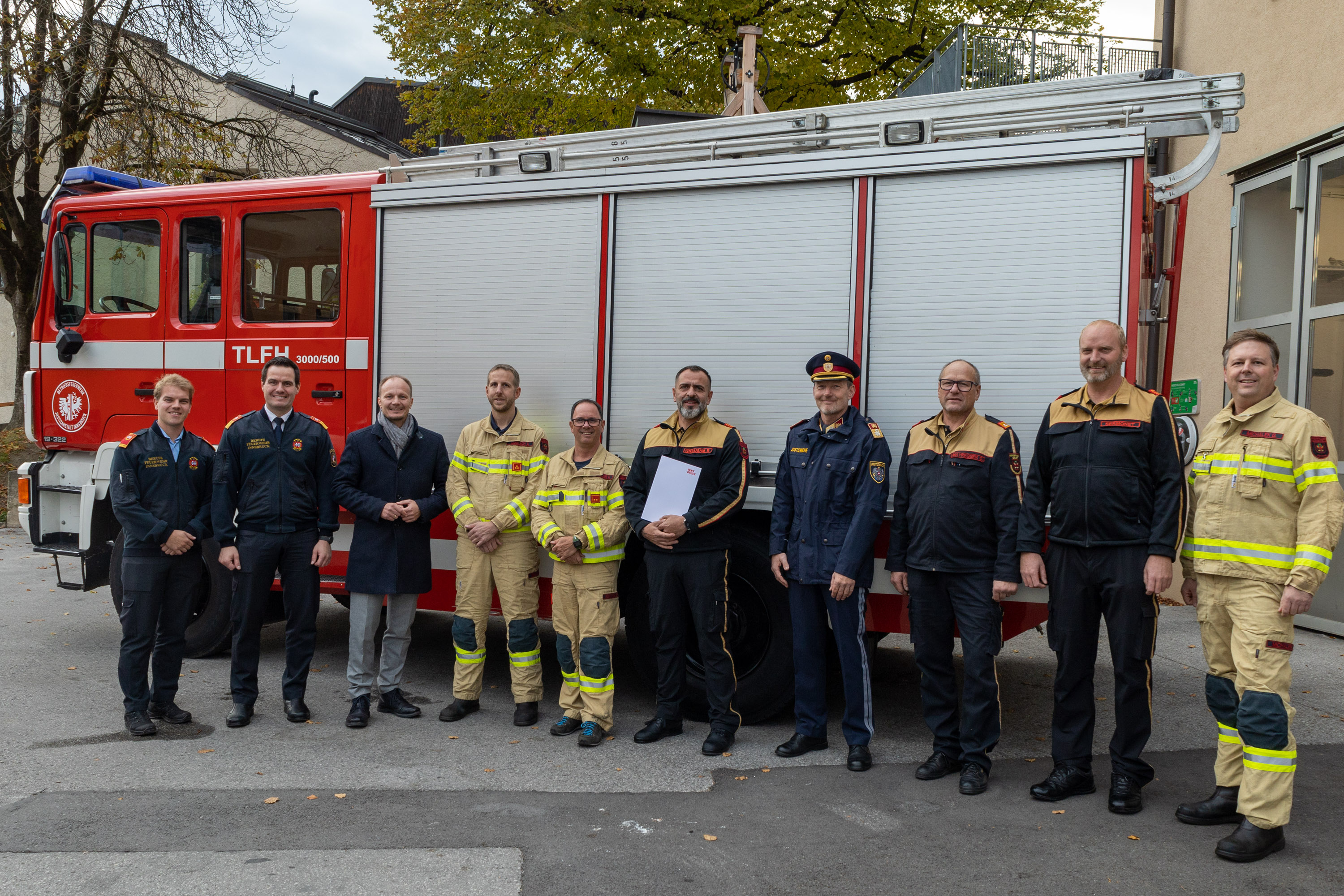 Feuerwehrmänner der Betriebsfeuerwehr der Justizanstalt, Christian Sermonet (2. v. r.) und Bernhard Grausam (5. v. r.), sowie Reinhard Potocnik, Leiter der Justizanstalt (4. v. r.), nehmen das Tanklöschfahrzeug der Freiwilligen Feuerwehr Hötting vor Ort entgegen.