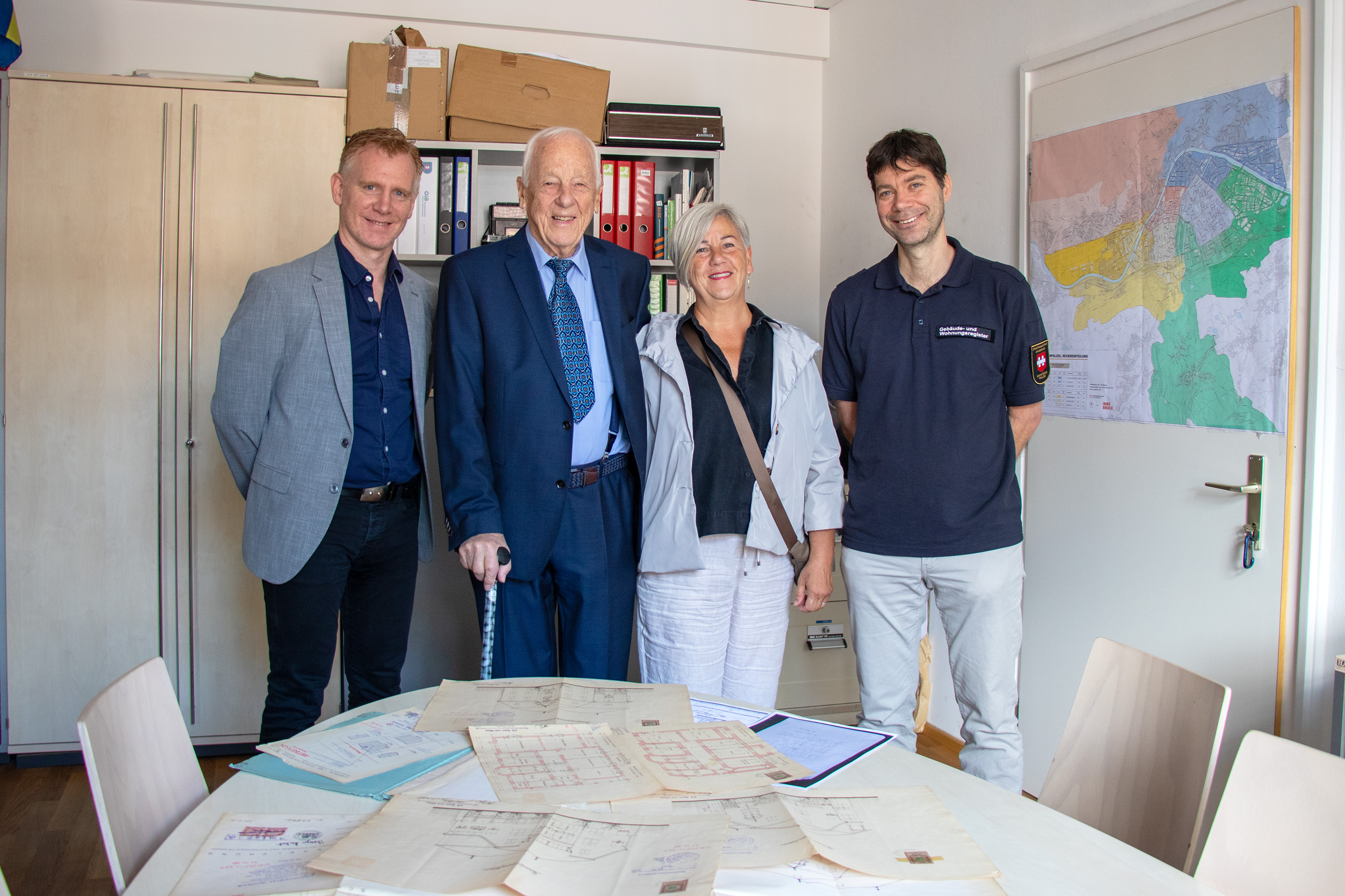 Ein Stück Innsbrucker Baugeschichte wurde heute im Amt Bau- und Feuerpolizei lebendig: Dem 94-jährigen Norbert Benzer wurden gemeinsam mit seiner Tochter Andrea Duplikate der historischen Bestandspläne seines Wohnhauses aus dem Jahr 1902 überreicht – gefertigt von der bis heute bestehenden Firma Huter & Söhne. Der rüstige Innsbrucker, der 1931 genau in jenem Haus in der Elisabethstraße geboren wurde, in dem er noch immer lebt, plant zum Abschluss seines Lebens eine Umbaumaßnahme im Gebäude: „Ich möchte meine Flügel noch ein wenig ausstrecken“, so Benzer mit einem Schmunzeln.
Gemeinsam mit Amtsvorstand Christian Kugler und Referent Manfred Hirsch vom Gebäude- und Wohnungsregister wurden die historischen Unterlagen eingehend studiert. Dabei hatte Herr Benzer so manche Anekdote aus fast einem Jahrhundert Hausgeschichte zu erzählen – von berühmten Untermietern bis hin zu einer einst verschwundenen Küche. Vielleicht wird man diese Geschichten bald in einem geplanten Podcast hören können, der Innsbrucker ZeitzeugInnen und ihre Erinnerungen zu Wort kommen lässt.