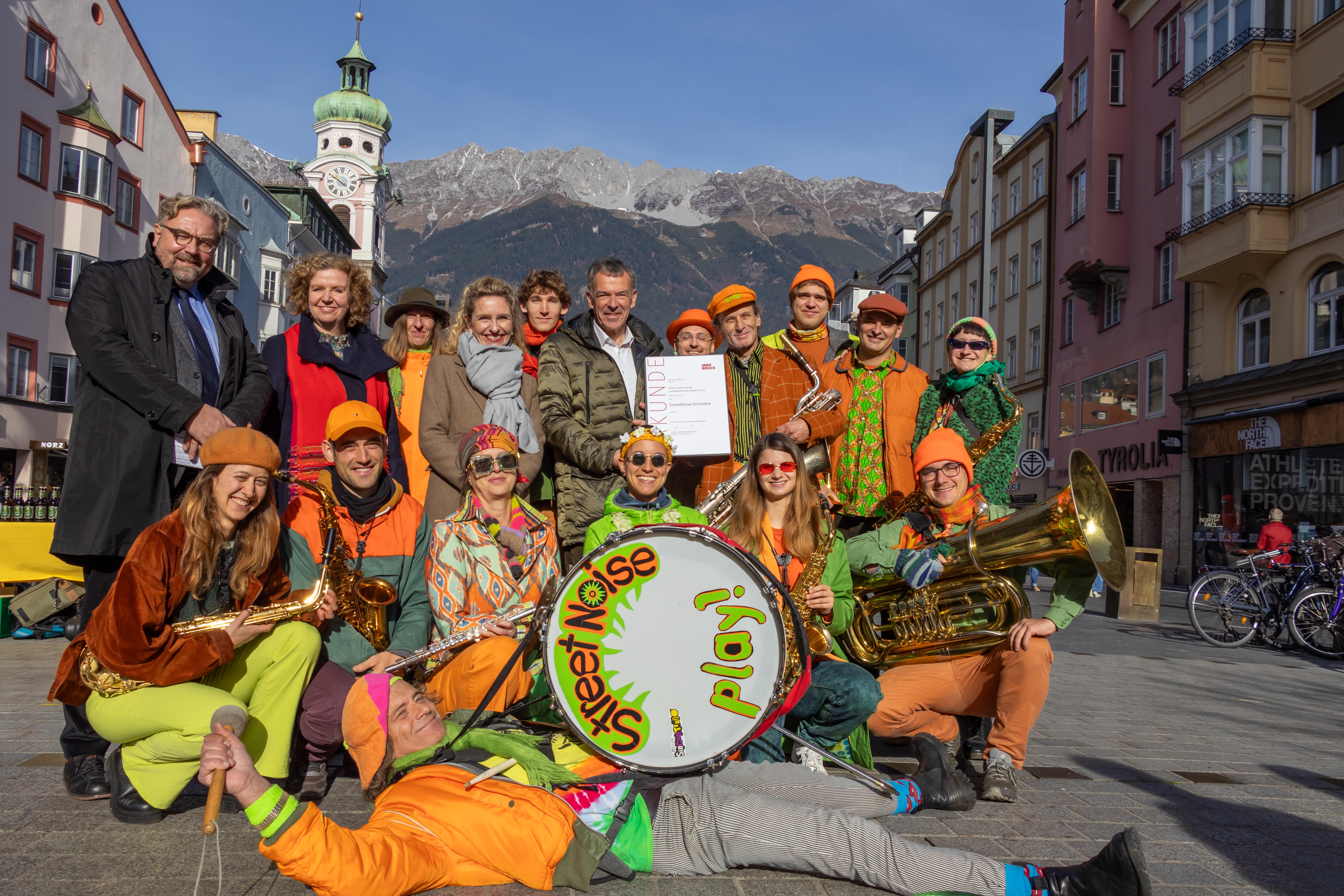 Bunt und laut: Der Arthur-Haidl-Preis der Stadt Innsbruck 2025 ging an das Innsbrucker StreetNoise Orchestra. Vizebürgermeister Georg Willi (Bildmitte), Magistratsdirektorin Gabriele Herlitschka (2. v. l.), Kulturamtsleiterin Isabelle Brandauer (4. v. l.) und Dirk Rupnow (Vizerektor für Personal an der Universität Innsbruck, links) freuen sich mit dem ehrenamtlichen Musikverein.
